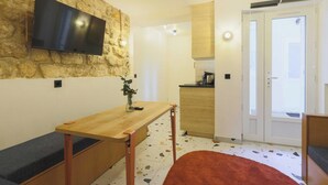 Un espace de vie compact doté d’un mur en pierre, d’un téléviseur fixé au mur, d’une kitchenette et d’une porte coulissante donnant sur un balcon.