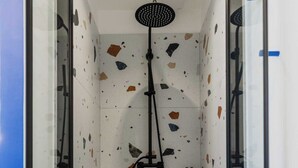 Un espace douche moderne doté d’une douche à pluie, de portes en verre et de carreaux au motif moucheté.
