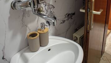 A bathroom with a white sink, a mirror, a glass shelf with toiletries, and a wooden door.