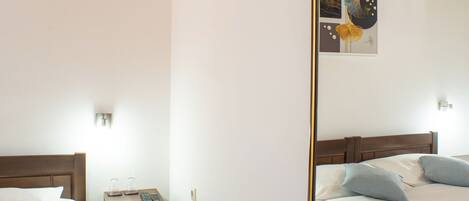 A bedroom with two beds, a nightstand, a mirror, and a wall-mounted light fixture.