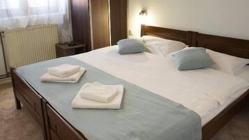 Cama bem arrumada com travesseiros, cabeceira de madeira e colcha azul claro. Há um radiador na parede e um quadro sobre a cama.