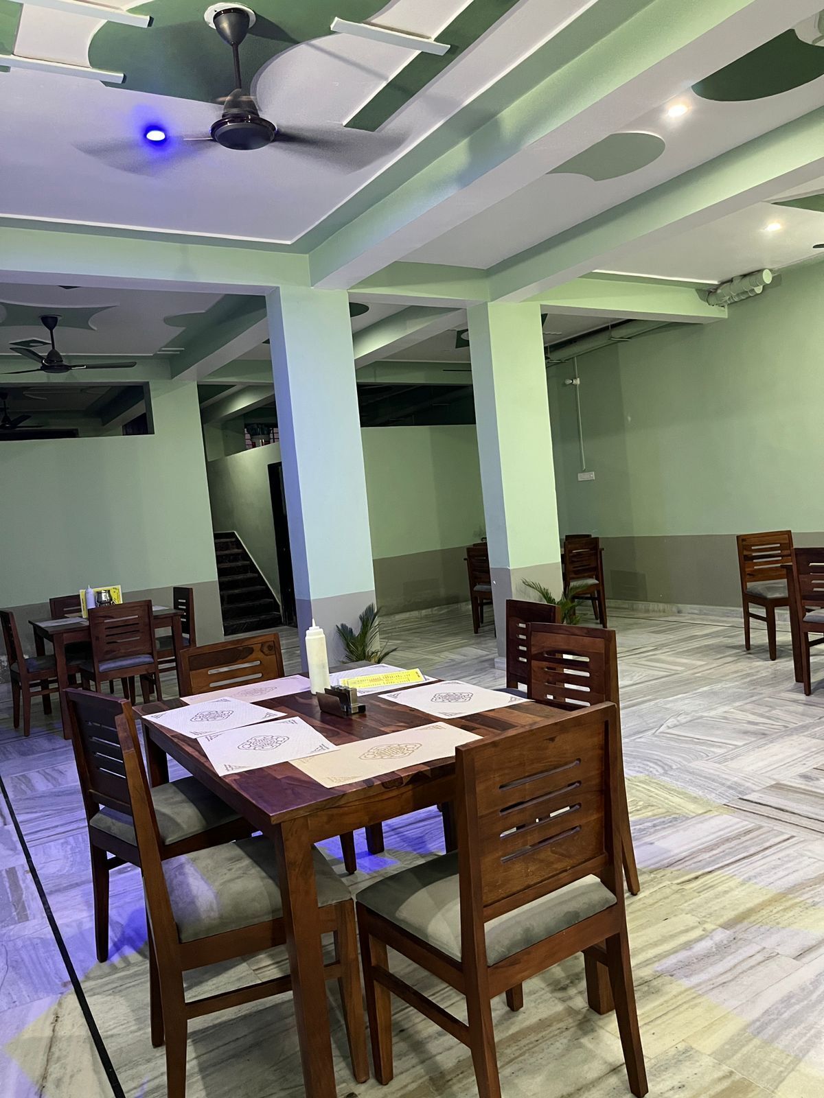 Uma sala de jantar com uma longa mesa de madeira, várias cadeiras e ventiladores de teto.