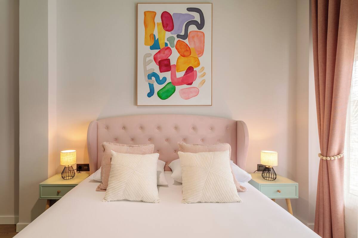 Una camera da letto con testiera trapuntata, due comodini con lampade, un letto con cuscini e un quadro astratto dai colori vivaci appeso alla parete.
