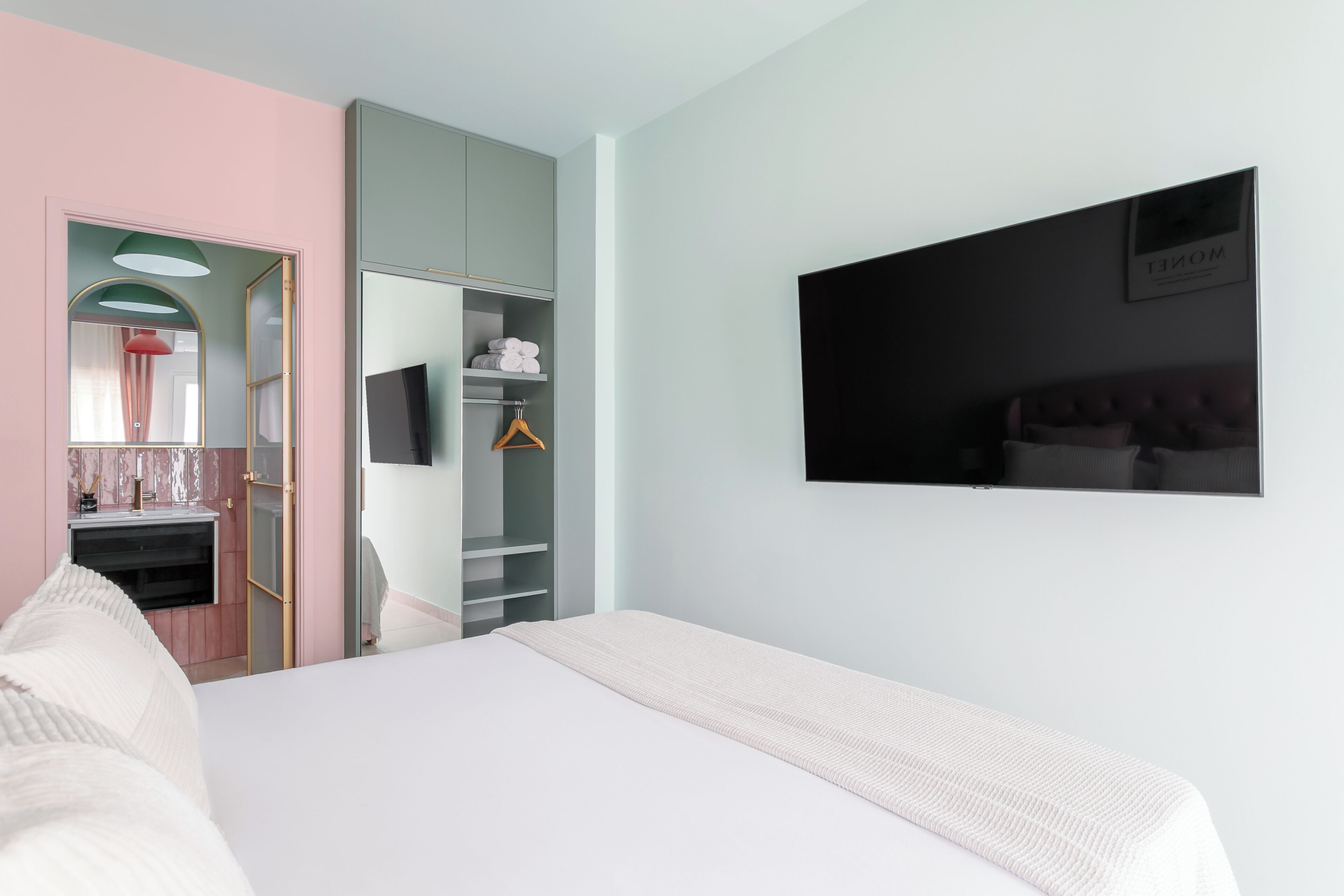 A bedroom with a bed, a wardrobe, a mirror, and a television on the wall.