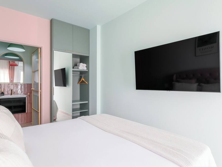 A bedroom with a bed, a wardrobe, a mirror, and a television on the wall.