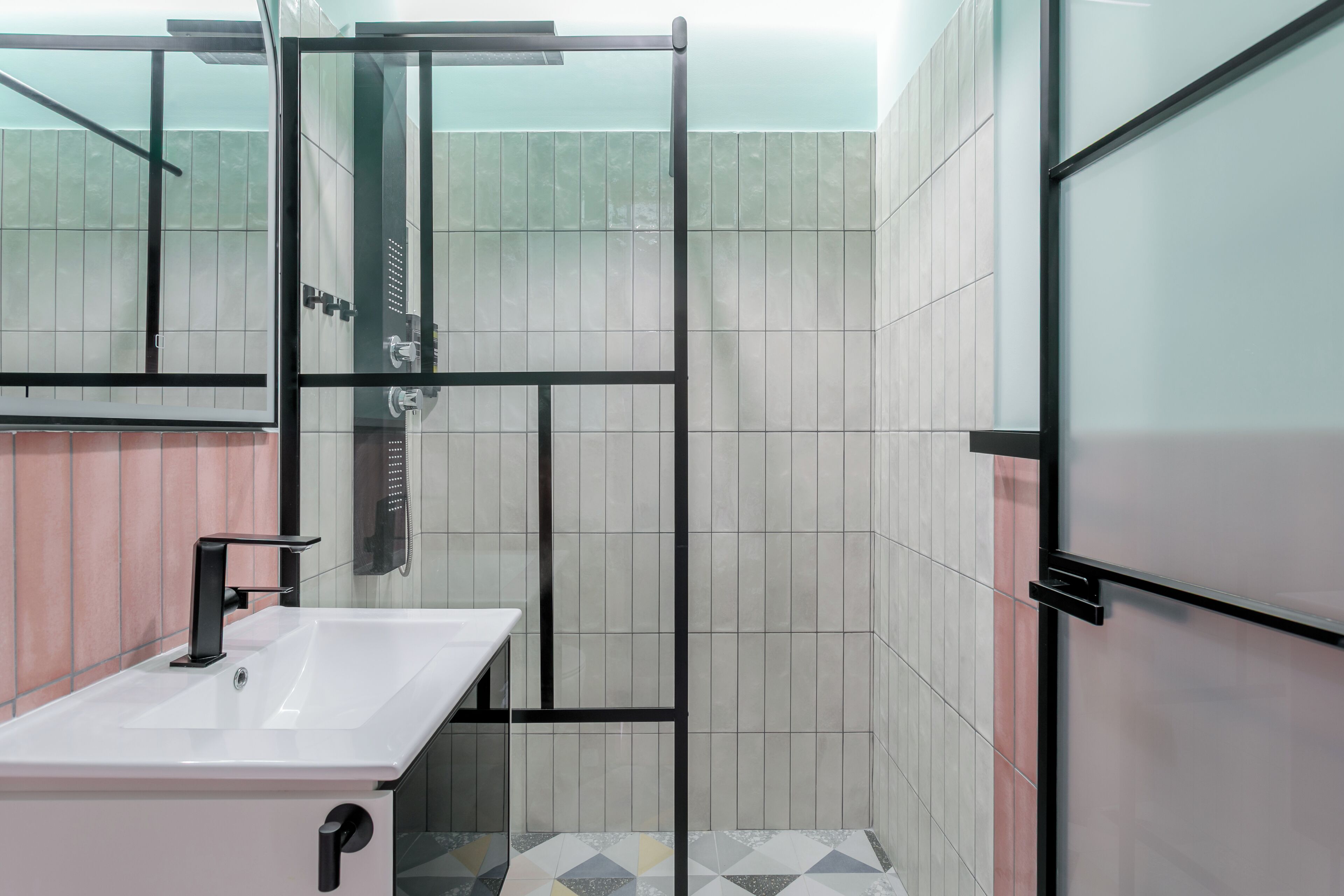 Un baño moderno con cabina de ducha de vidrio, lavamanos blanco y paredes con azulejos.