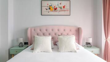 Una cama bien hecha con un cabecero capitonado, dos mesitas de noche con lámparas y una obra de arte abstracta enmarcada en la pared.