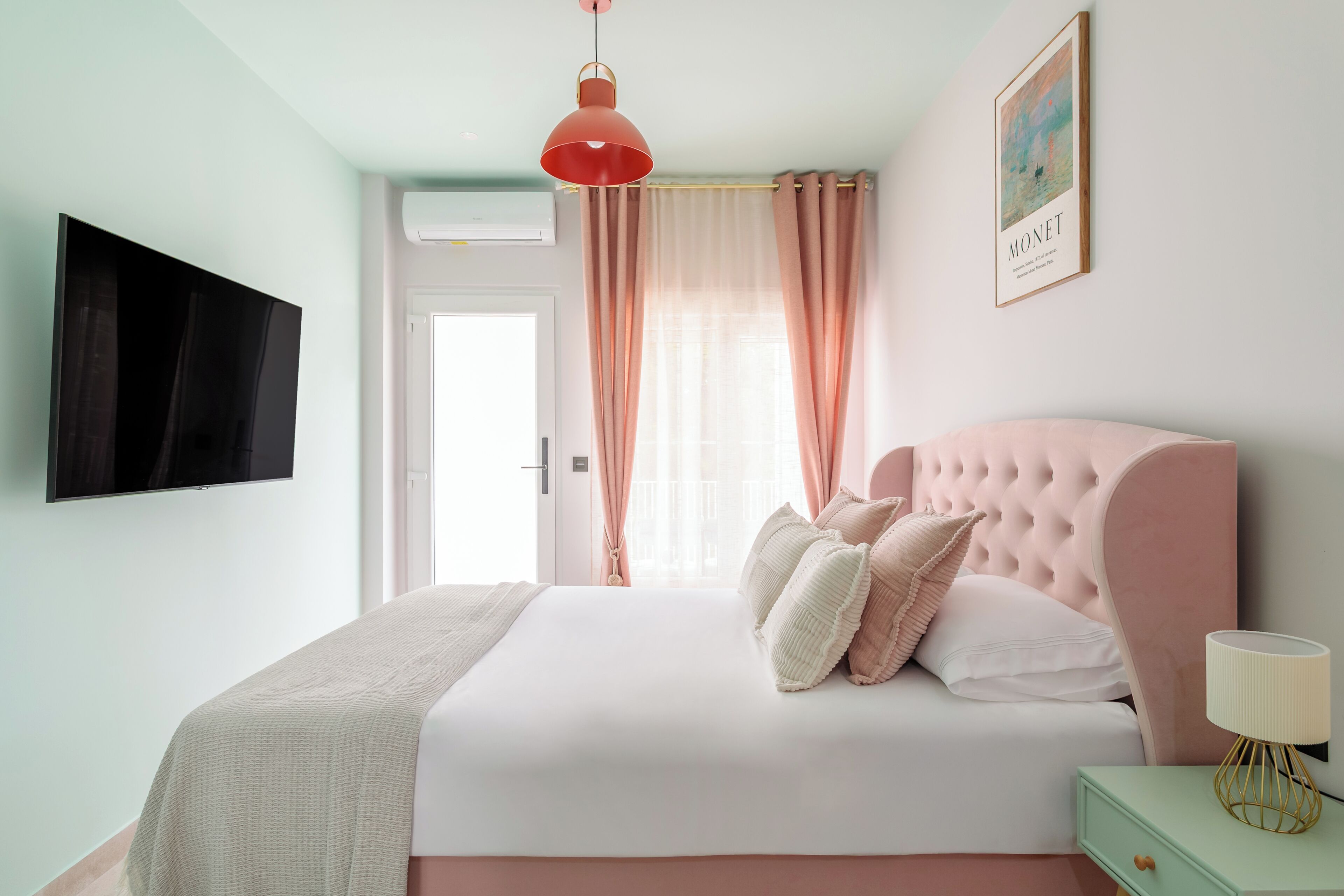 A bedroom with a large bed, a television on the wall, a window with curtains, and a framed picture.