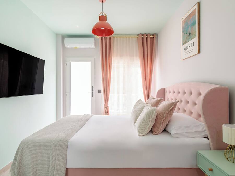 Quarto com cama grande, televisão na parede, janela com cortinas e um quadro emoldurado.