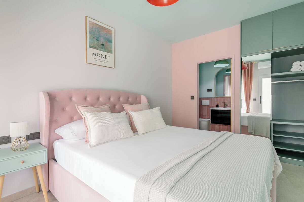 Una camera da letto con una testiera rosa capitonné, biancheria da letto bianca e un quadro appeso al muro.
