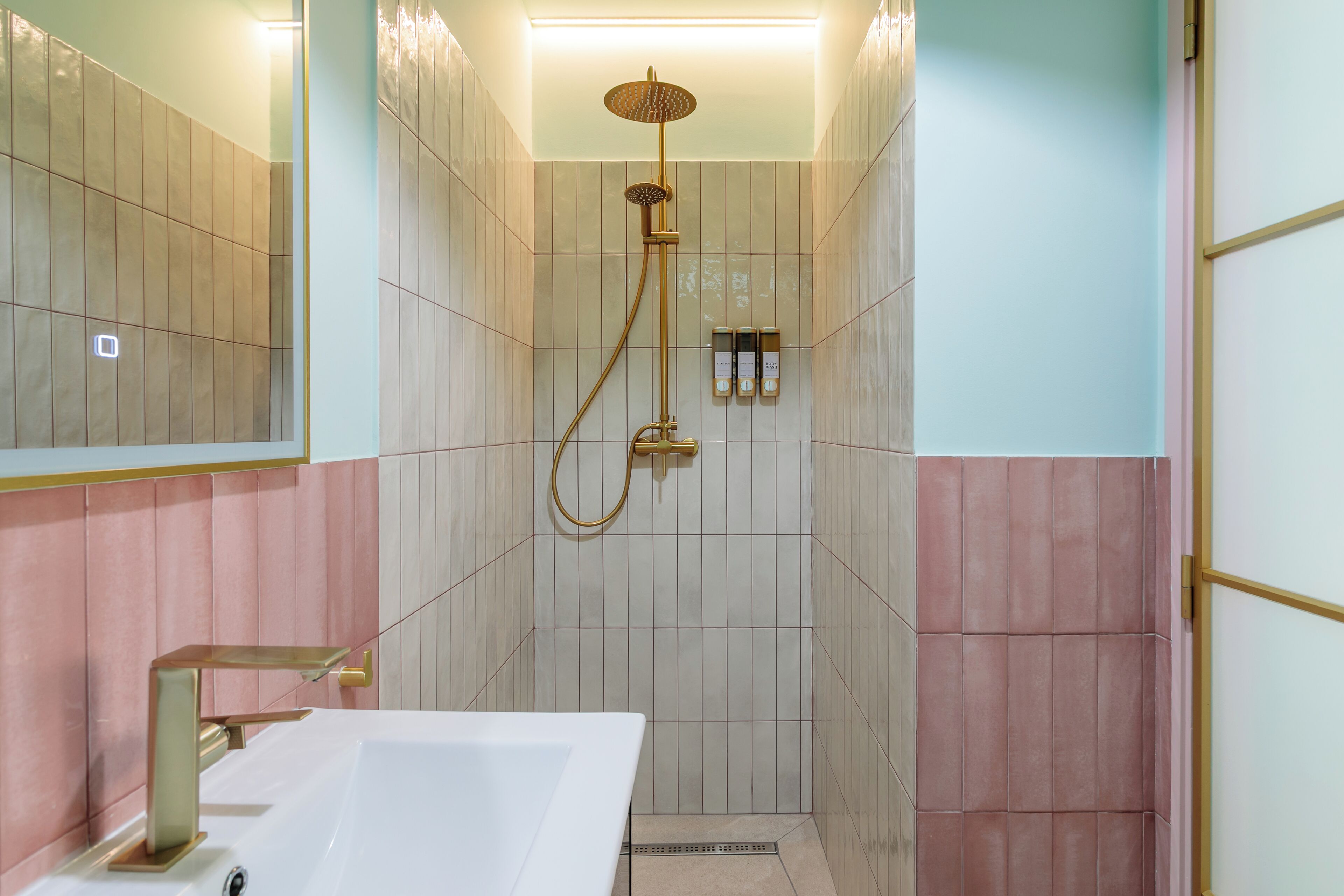Un bagno con un lavandino bianco, una doccetta dorata e uno specchio.