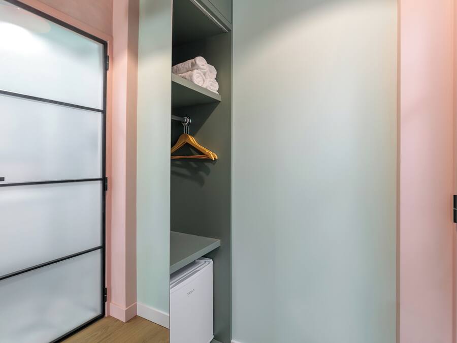 Un armario vestidor con un mueble de almacenamiento blanco, un perchero de madera y un electrodoméstico blanco.