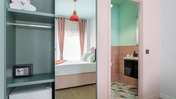 Quarto moderno com cama, guarda-roupa, pequeno frigorífico e casa de banho com sanita e lavatório.