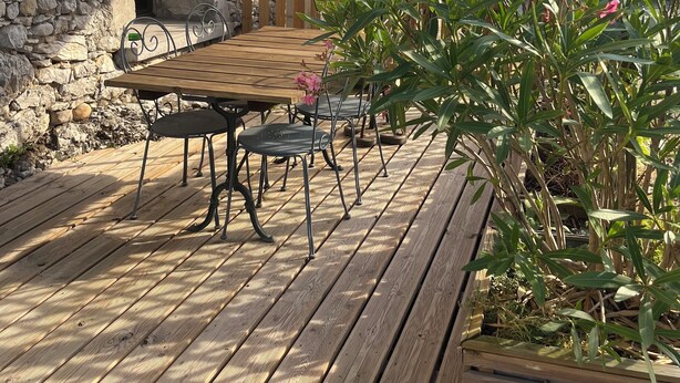 A wooden deck with a table and chairs, a stone wall, and a large umbrella. - Apartment with terrace for 2 people Le nid du phénix 38 in the countryside (Arandon-Passins)