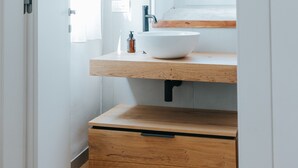 Ein modernes Badezimmer mit einem Holzwaschtisch, einem runden Spiegel und einem Fenster mit Tageslicht.