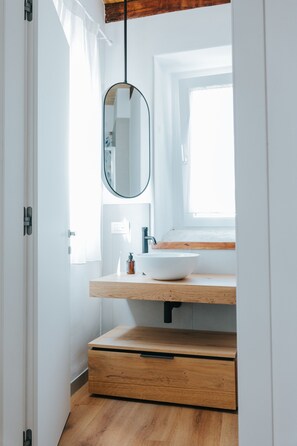 Ein modernes Badezimmer mit einem Holzwaschtisch, einem runden Spiegel und einem Fenster mit Tageslicht.