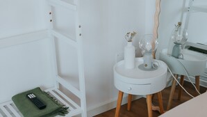 A white room with a white shelf, a small white table with a vase and a glass, and a remote control on a green cloth. - Room 'Vista Sul Castello' with Wi-Fi (Cison di Valmarino)