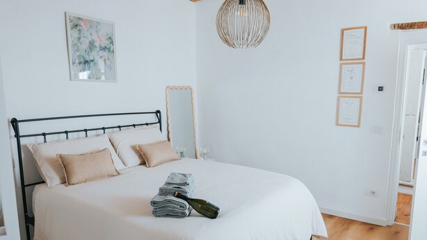 A neatly made bed with pillows, a folded towel, and a bottle, a hanging light fixture, and a framed picture on the wall. - Room 'Vista Sul Castello' with Wi-Fi (Cison di Valmarino)
