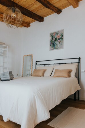 Ein Schlafzimmer mit einem Bett, einer Holzbalkendecke, einem Spiegel und einem Bild an der Wand.
