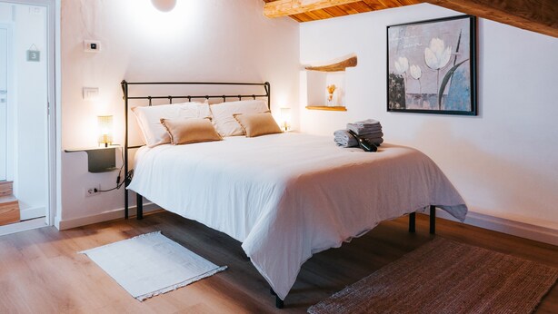 A bedroom with a bed, bedside lamps, a painting, and a wooden ceiling. - Room 'With Castle View' with Wi-Fi and Air Conditioning (Cison di Valmarino)