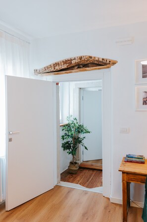 A hallway with a wooden floor, a white door, a potted plant, and a small table with books. - Room 'Rustic Charm' with Wi-Fi (Cison di Valmarino)