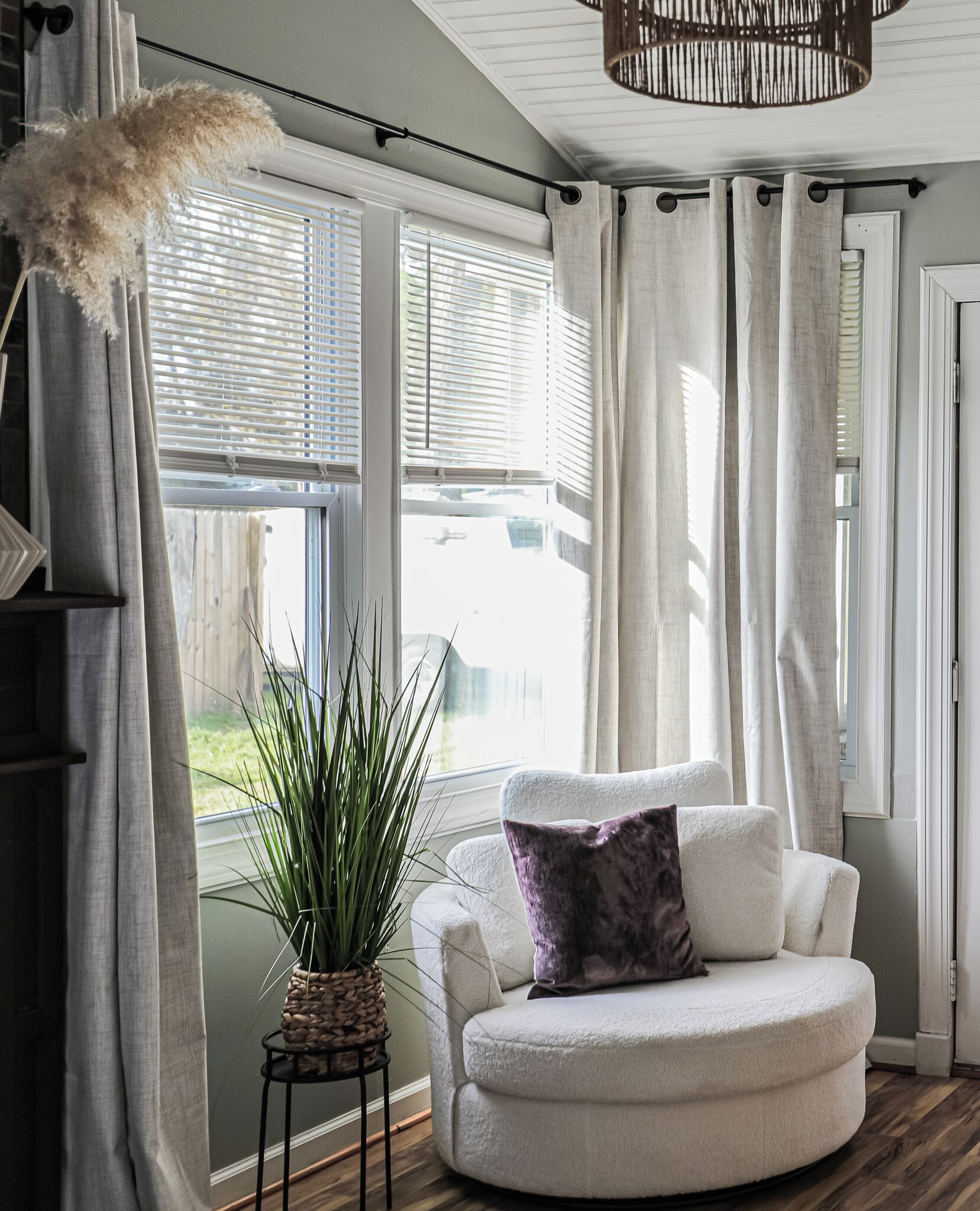 A cozy living room with a white sofa, a potted plant, and a hanging light fixture.