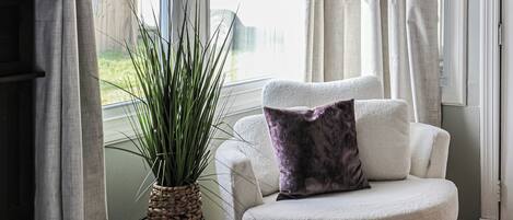 A cozy living room with a white sofa, a potted plant, and a hanging light fixture.