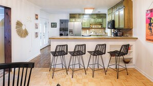 Une cuisine avec un coin bar, un plancher en bois et quatre tabourets de bar noirs.