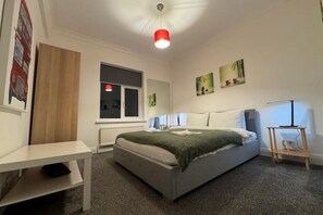 Un dormitorio con cama, mesitas de noche, una ventana y obras de arte en las paredes.
