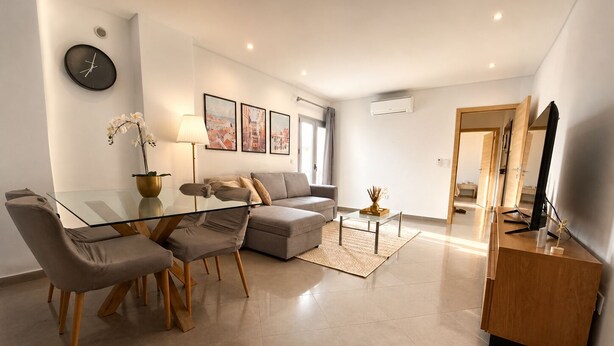 A modern living room with a glass dining table, grey sofas, a coffee table, and a TV stand. - Fatima Experience 50 meters from the Sanctuary of Fátima (Fátima)