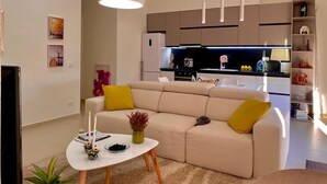 A modern living room with a beige sofa, a white coffee table, and a kitchen in the background.