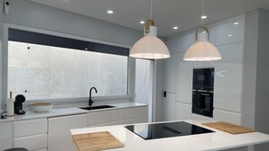 Una cocina moderna con un ventanal grande, armarios blancos, un lavamanos negro y dos lámparas colgantes.