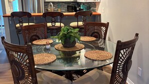 A dining area with a glass table surrounded by wicker chairs, a central potted plant, and woven placemats.