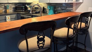 A modern kitchen with white cabinets, a wooden bar counter, and two ornate chairs.