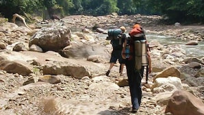 A rocky riverbed with hikers carrying backpacks. - Refugio los Volcanes (Cuevas)