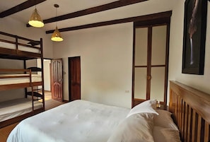 A room with bunk beds, a wooden door, a bed with white bedding, and a pendant light.