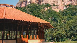 A building with a tiled roof and large windows, surrounded by lush greenery and a mountainous backdrop. - Refugio los Volcanes (Cuevas)