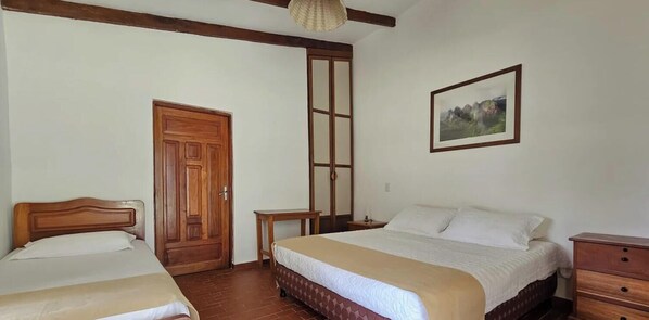 Ein Schlafzimmer mit zwei Betten, einer Holztür, einem kleinen Tisch, einem Nachttisch und einem gerahmten Bild an der Wand.