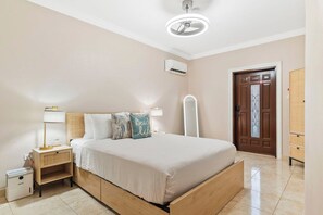 A bedroom with a bed, bedside table, lamp, and an air conditioning unit.