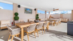 Un espace de restauration en plein air avec une longue table en bois, des chaises en osier et un canapé.