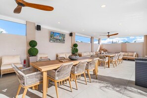 An outdoor dining area with a long wooden table, wicker chairs, and a sofa.