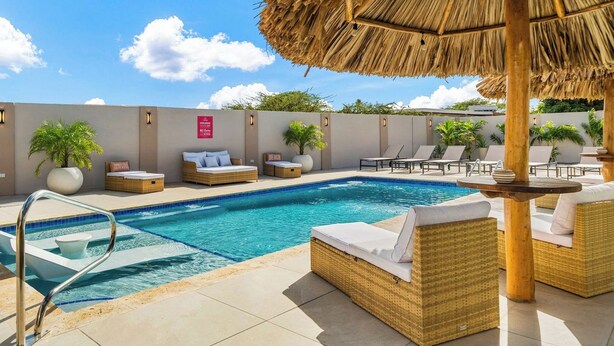 Un espace piscine avec des chaises longues, un parasol en chaume et un panneau indiquant une vue sur la plage.