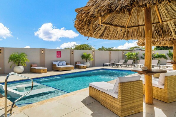 A pool area with lounge chairs, a thatched umbrella, and a sign indicating a beach view.