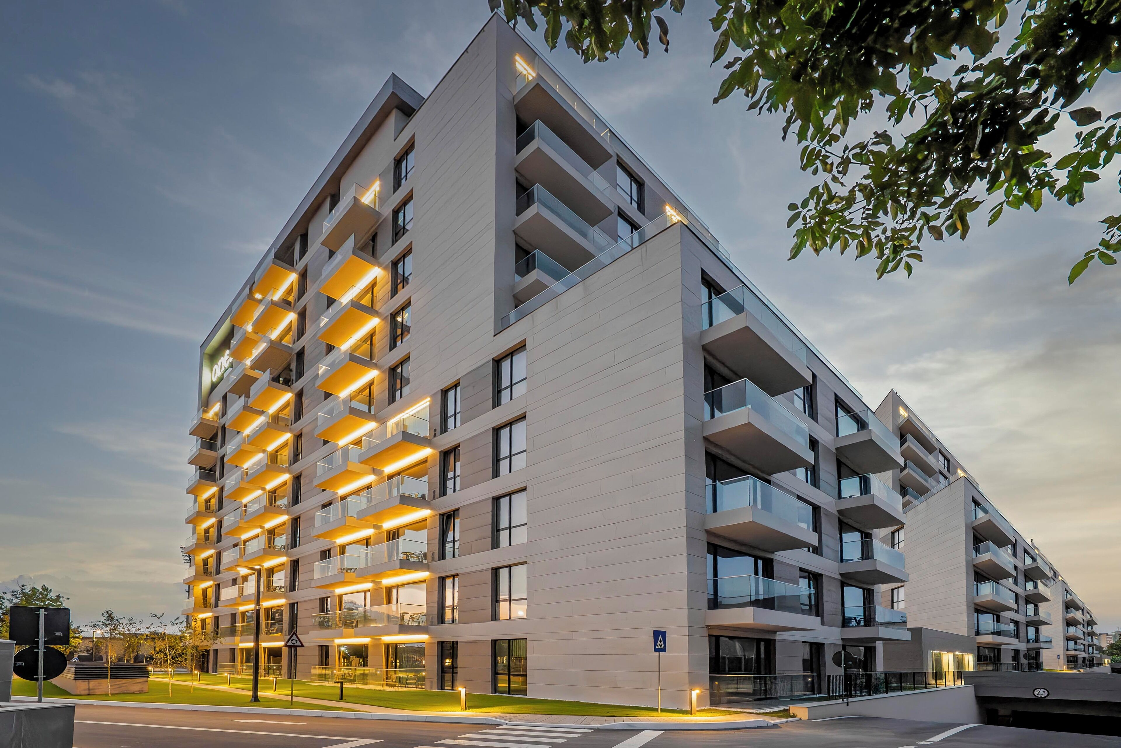 A modern multi-story residential building with balconies, large windows, and a well-lit facade.