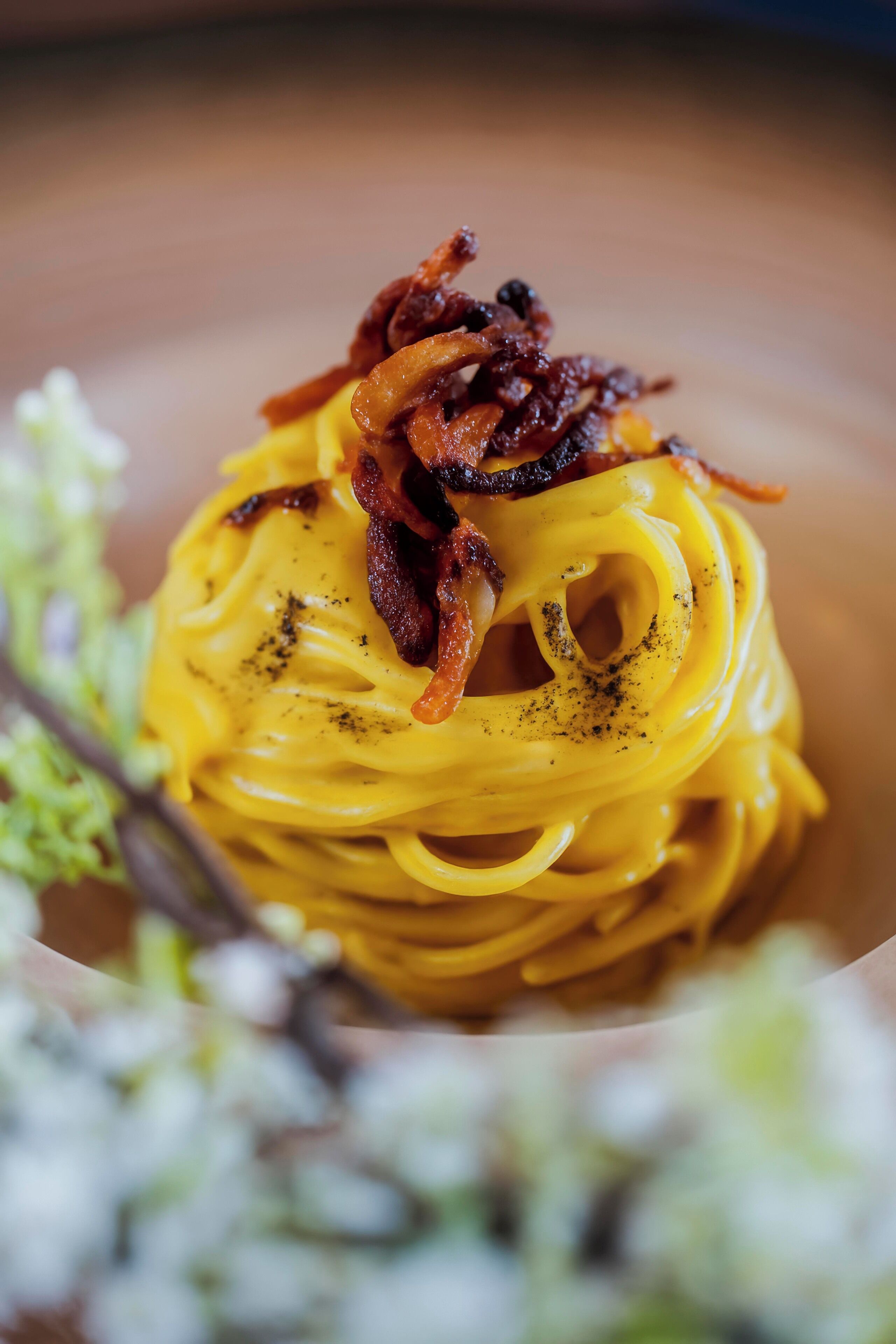 A close-up of a pasta dish with a creamy yellow sauce, topped with caramelized onions and black pepper.