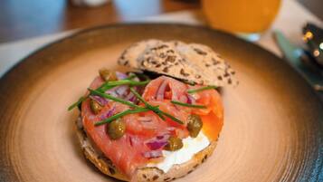 A breakfast plate with a bagel topped with smoked salmon, cream cheese, chives, and capers, accompanied by a glass of orange juice.
