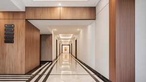 A modern hotel corridor with a wooden panel wall, a signboard with room names, and a reflective floor. - ONE66 (Brașov)