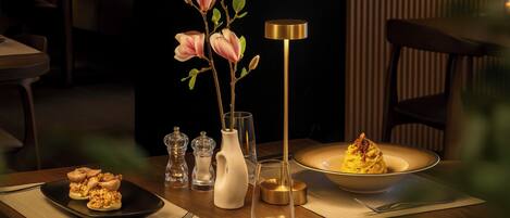 A dining table with a plate of food, a vase with flowers, and a tall lamp.