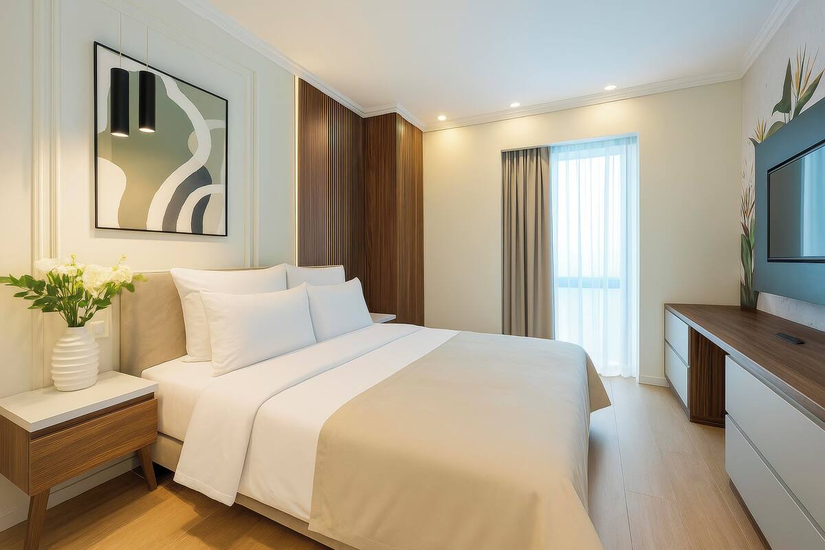 Habitación de hotel moderna con una cama grande, una mesita de noche con un florero, un televisor en un mueble de madera y un cuadro abstracto de gran tamaño en la pared.