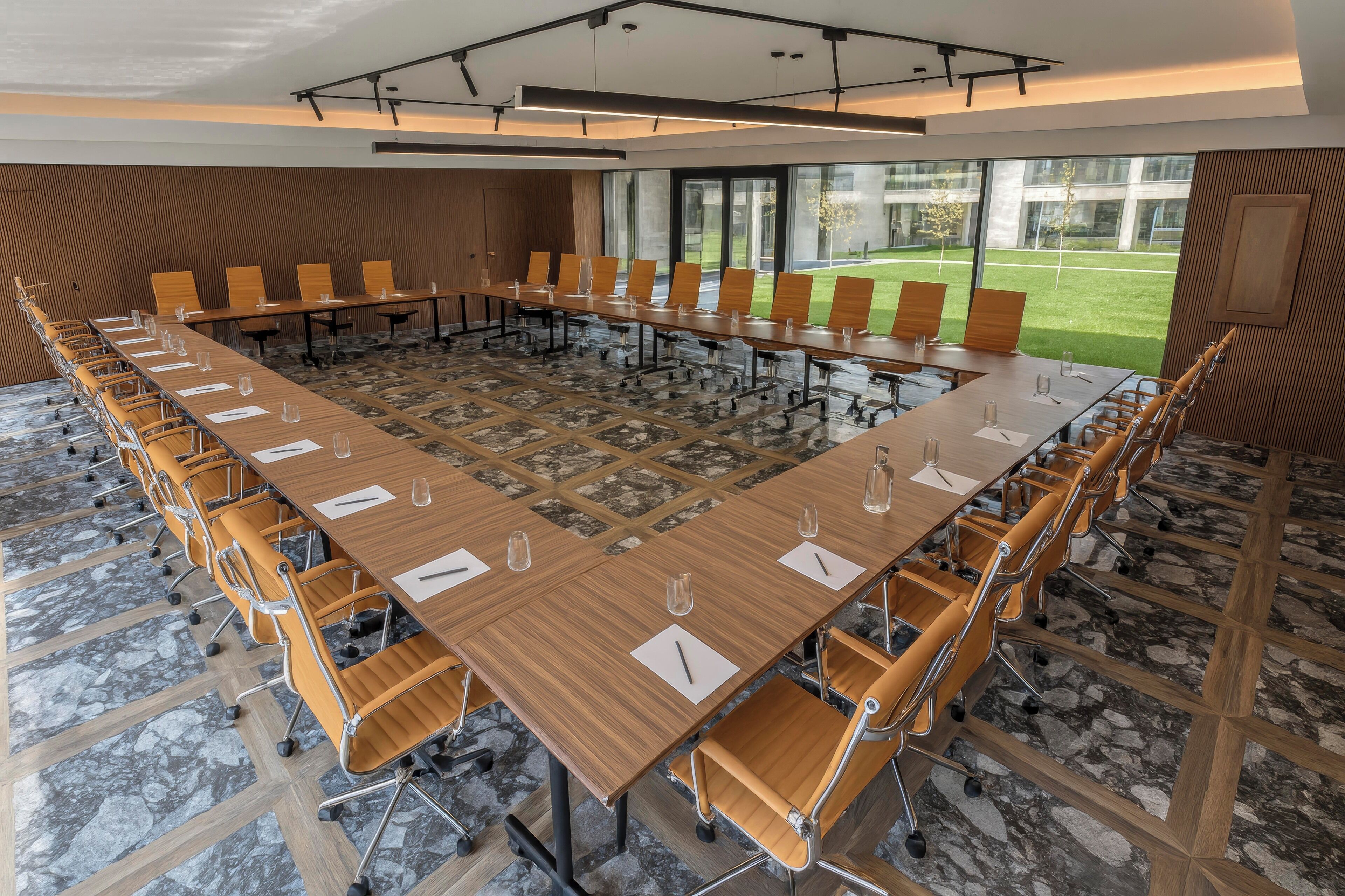 A conference room with a long table, multiple chairs, and a view of a grassy area through large windows.
